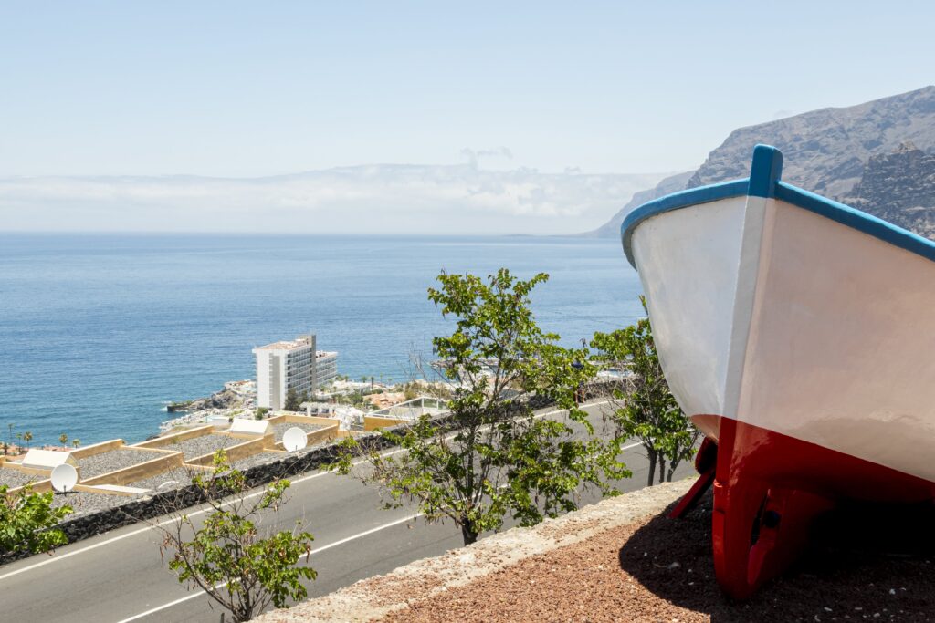 A scenic coastal view in Cyprus featuring a white and red boat on a hillside overlooking the sea, with a modern building and lush greenery in the background.
