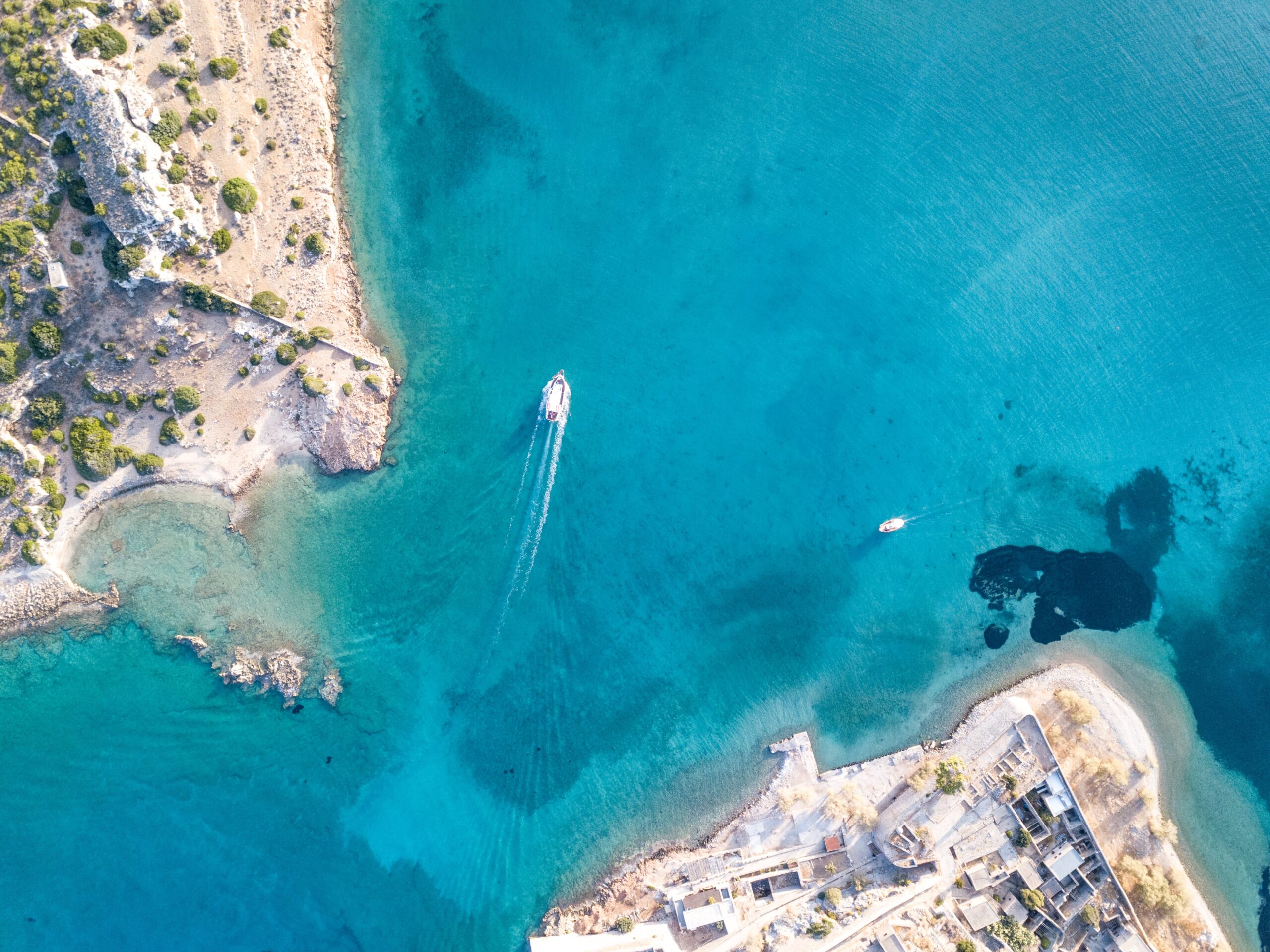 Aerial view of the Cyprus coastline featuring clear turquoise waters, rugged cliffs, and boats cruising along the shore.