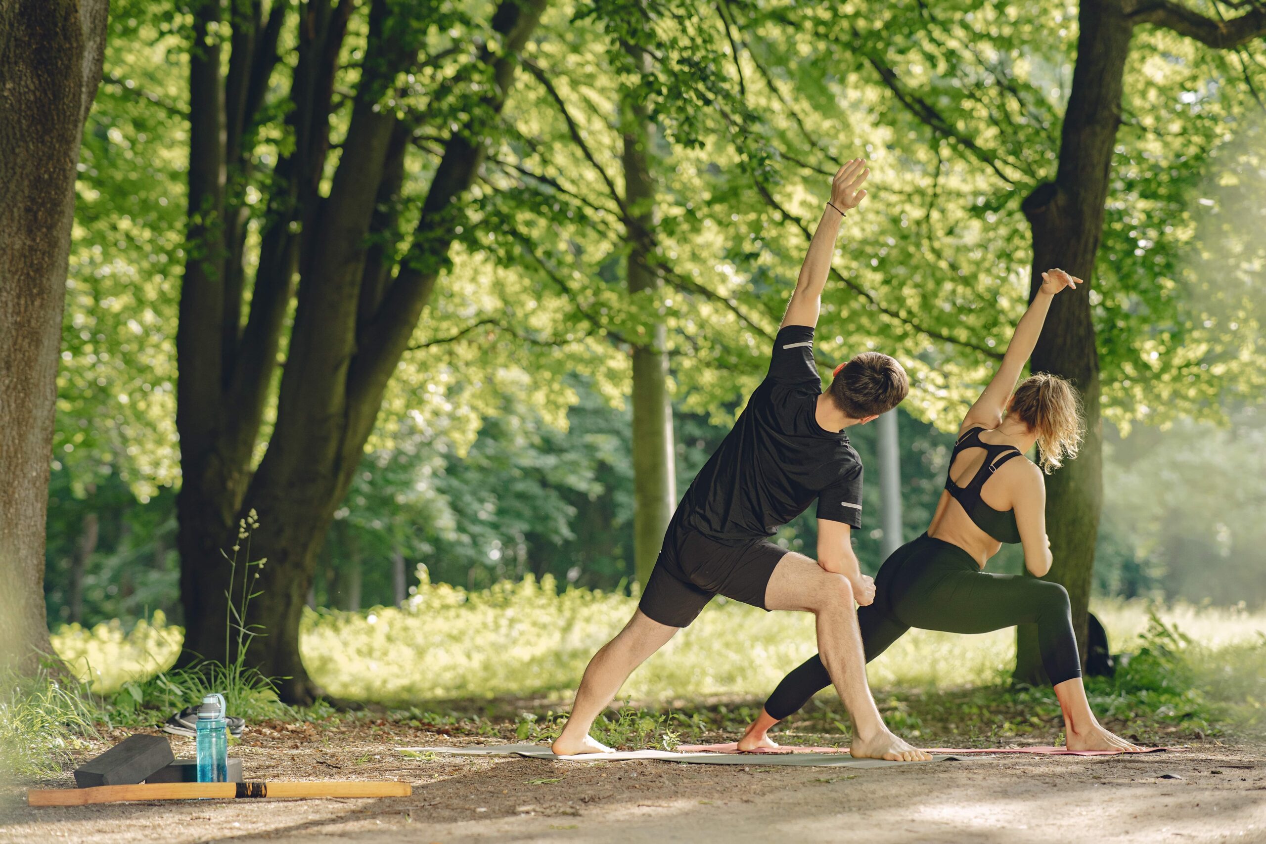 A man and a woman practicing yoga in a serene forest setting on a sunny day.