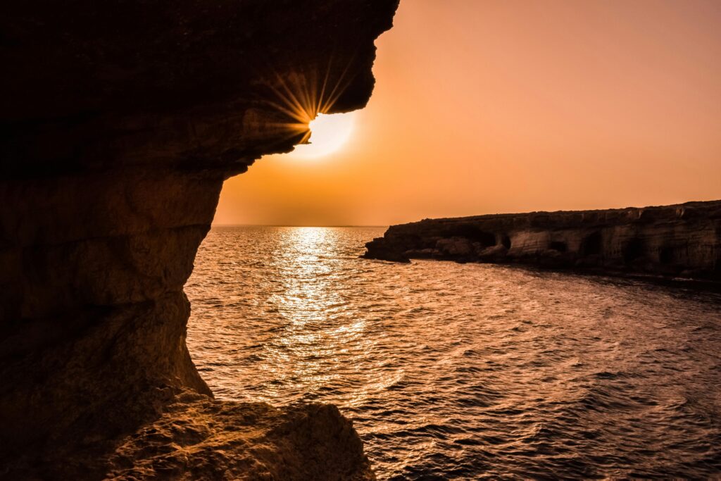 Sunset over Cyprus sea caves with golden light reflecting on the ocean and rocky cliffs.