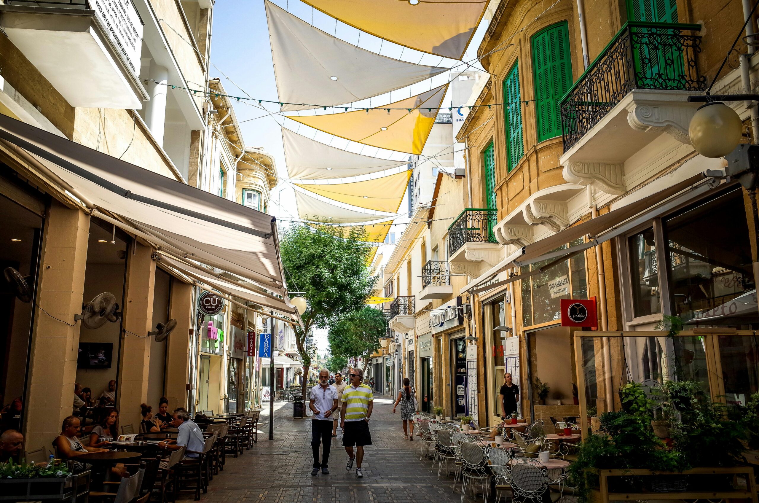 A vibrant street in Nicosia, Cyprus, with cafes, historic buildings, and people walking under decorative sunshades.