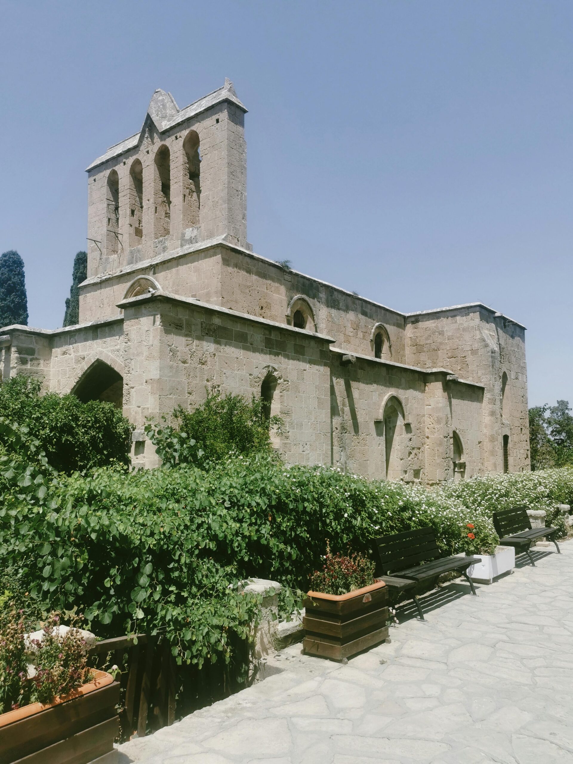 Bellapais Abbey in Cyprus, a medieval stone monastery surrounded by greenery and benches on a sunny day.