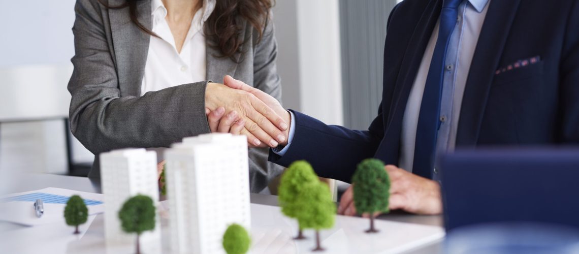 Business professionals shaking hands over a real estate model with miniature buildings and trees