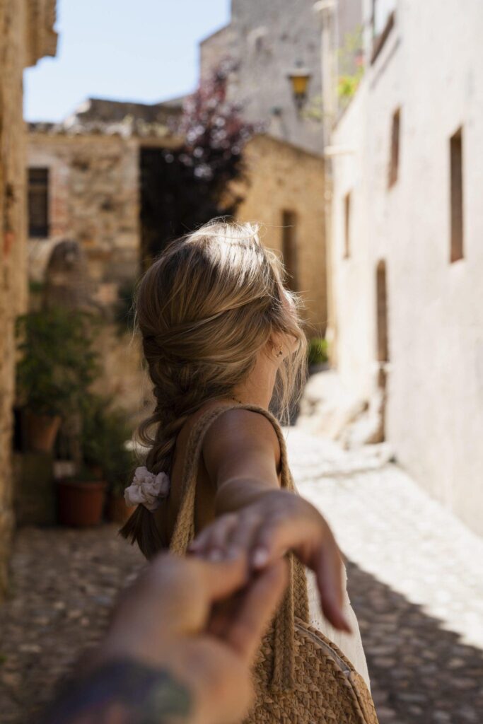 “Woman walking through a sunlit historic Mediterranean alley, holding someone’s hand, with stone buildings and cobblestone streets — Larnaca Cyprus lifestyle scene.”