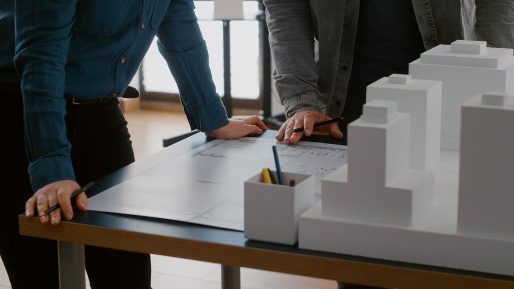 Professionals reviewing architectural plans beside a building model, representing oroklini property planning and development.